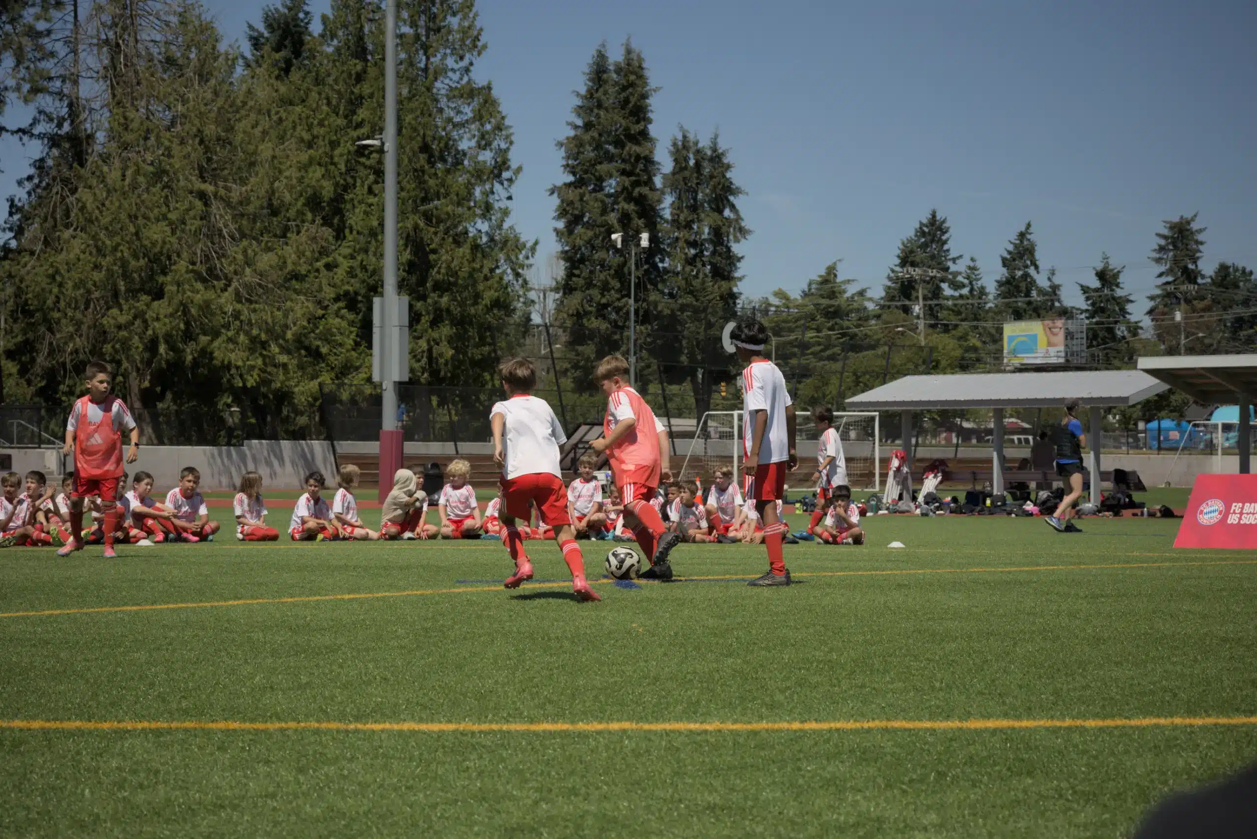 A group of children practicing ball control during a training session, demonstrating the stopper position in soccer on an artificial turf field.